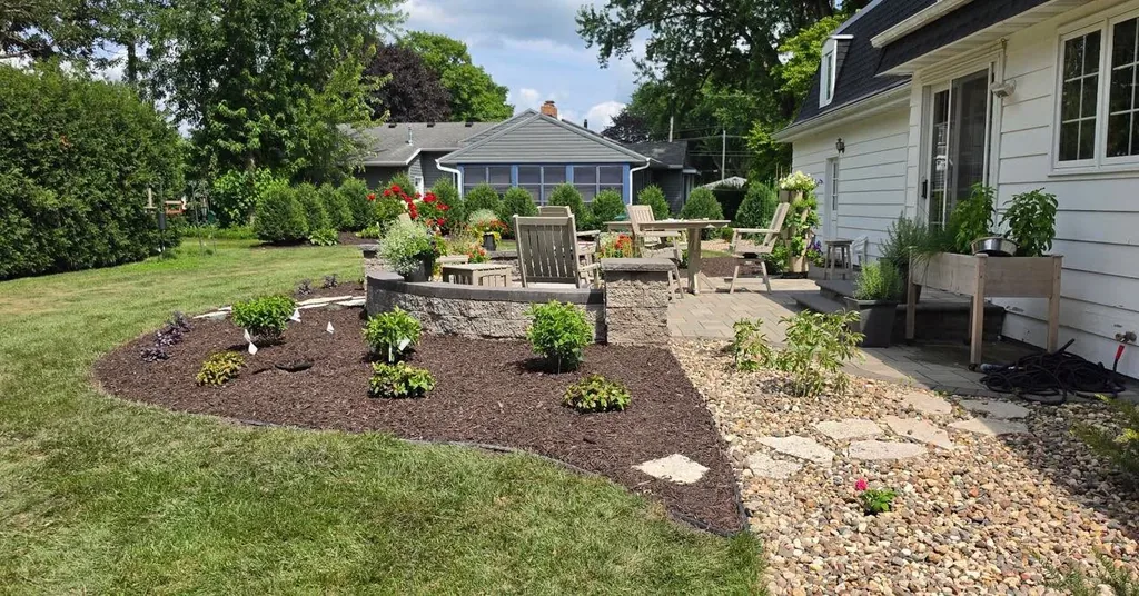 New planting bed with shrubs, mulch, and a stone path beside a house