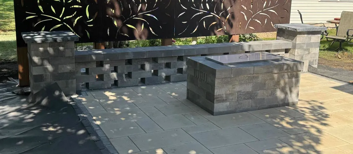 Gas fire feature with a block surround on a paver patio, backed by a block wall and metal privacy panels