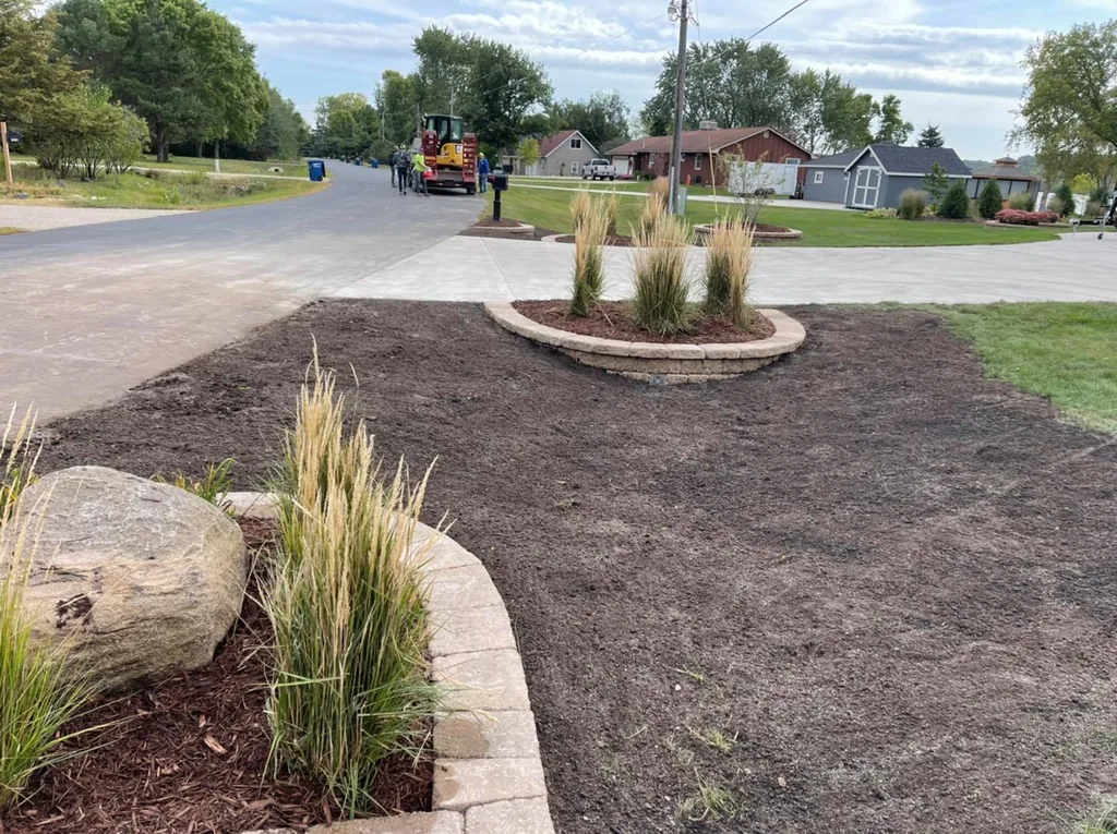 New planting bed with ornamental grasses and a boulder beside a block-edged ring bed