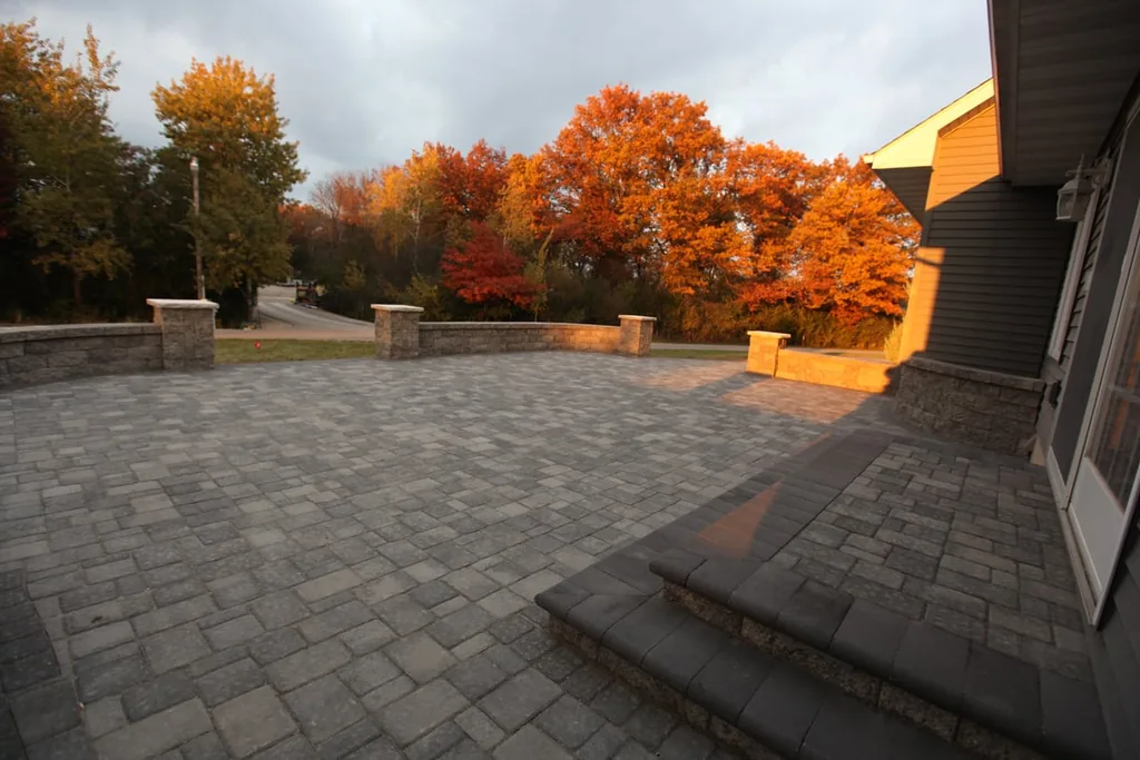Paver patio with wide steps up to the house and fall trees behind it